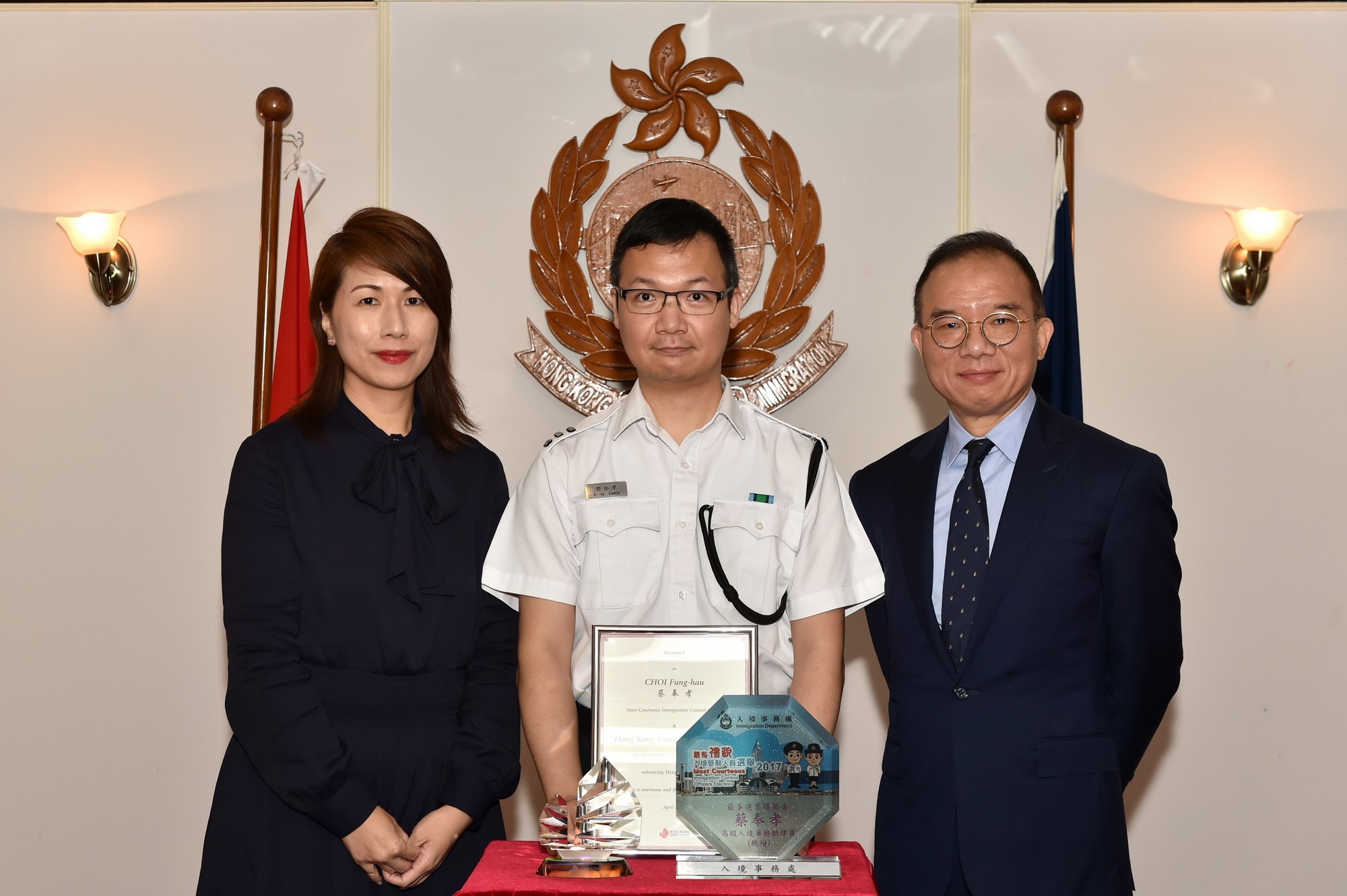 The General Manager of Corporate Affairs of the Hong Kong Tourism Board, Ms Cynthia Leung (left), and the Director of Immigration, Mr Tsang Kwok-wai (right), present awards and a souvenirs to the most courteous Immigration control officer, Mr Choi Fung-hau, today (April 24).